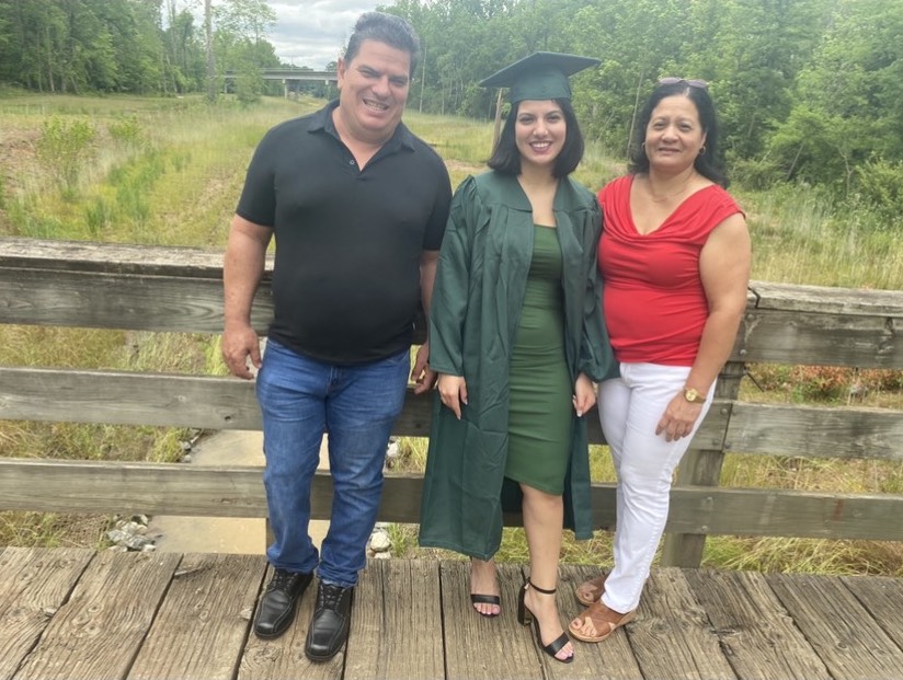 Elianet Hernandez Santana in undergraduate cap and gown and her parents standing on a bridge located on the UNC Charlotte main campus 